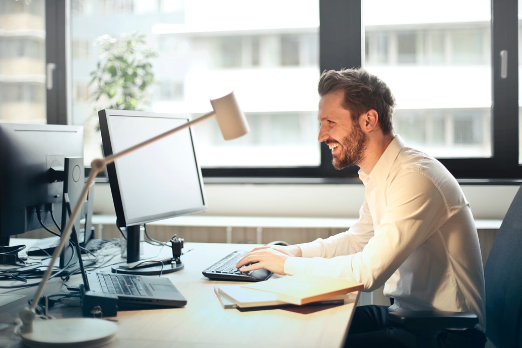 caucasian male sitting on a desk smiling as he works on his computer